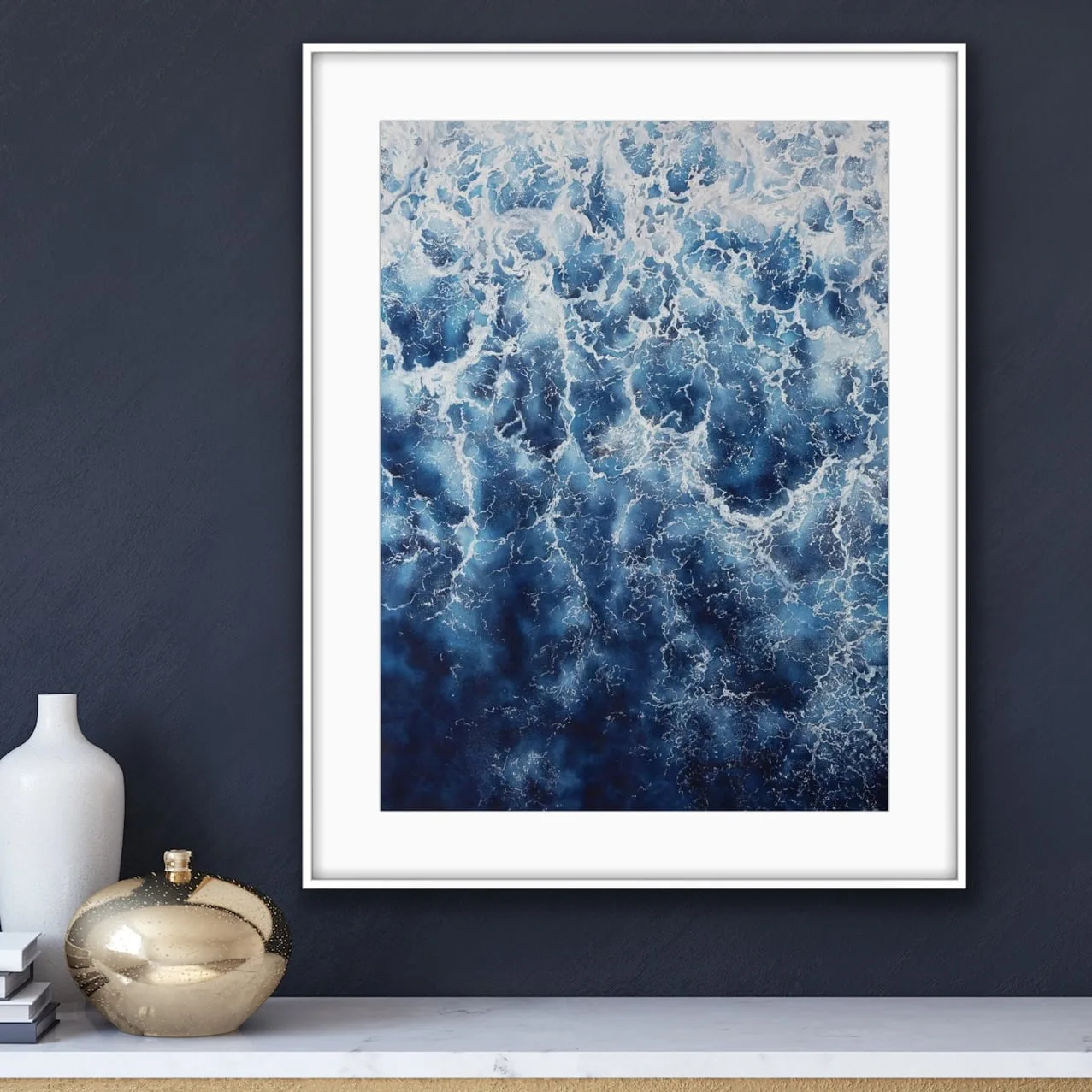 Framed abstract ocean wave painting ‘Deep Blue Sea’ above the commode in a modern living room, featuring rich blues and foam for an elegant touch.