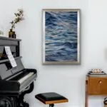 "Evening Mood" watercolor seascape framed above a piano in a living room, blending soft blues and grays to create a peaceful ocean scene that complements the tranquil ambiance of the space