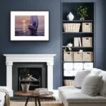 "Calmness" original watercolor sailboat painting elegantly framed and displayed above a fireplace, featuring a peaceful yacht on calm sunset waters—adding serene nautical charm to coastal-inspired living spaces.