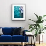 "Summer Memories" watercolor painting framed above a sofa in a modern living room, adding a serene coastal touch with a yacht sailing on calm sea waters.