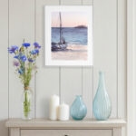 Sunset ocean watercolor painting with sailing boat framed and displayed in coastal living room, nautical seascape wall art for beach house decor, ocean lover gift idea, calming original boat artwork for sea-themed interior.
