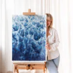 Kateryna Nazarenko in her studio with 'Deep Blue Sea' abstract ocean painting, emphasizing the rich blue tones and foamy waves.