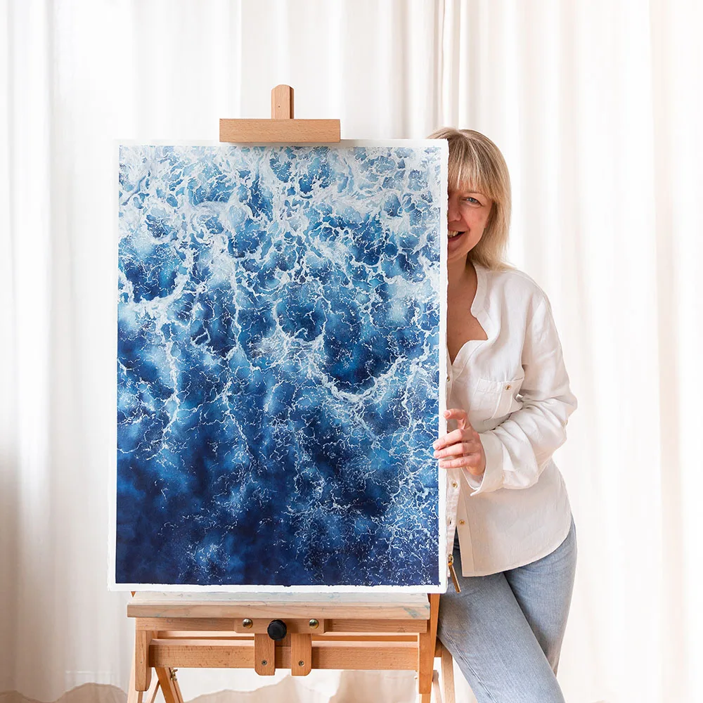 Kateryna Nazarenko in her studio with 'Deep Blue Sea' abstract ocean painting, emphasizing the rich blue tones and foamy waves.