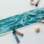 'Sparkles on Turquoise Water' in progress on Kateryna Nazarenko's studio table, with soft watercolor washes blending into vibrant turquoise tones, surrounded by brushes and sketch references.