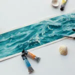 'Sparkles on Turquoise Water' in progress on Kateryna Nazarenko's studio table, with soft watercolor washes blending into vibrant turquoise tones, surrounded by brushes and sketch references.