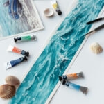 Close-up of 'Sparkles on Turquoise Water' being painted on a studio table, capturing delicate brushstrokes and shimmering layers of turquoise hues in the creative process.