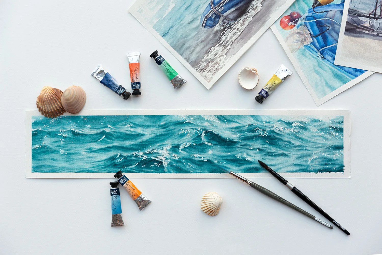 ‘Sparkles on Turquoise Water’ in progress on a table in Kateryna Nazarenko’s art studio, surrounded by watercolor brushes and palettes, showcasing the delicate layers of turquoise and shimmering light reflections taking shape.