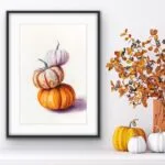 Autumn pumpkin watercolor painting styled above shelf with cozy fall decorations.