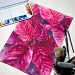 Magenta Poinsettia watercolor painting displayed on a desk surrounded by paints and brushes, reflecting the creative atmosphere of an artist's workspace, perfect for adding vibrant, festive energy to your studio.