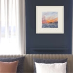 Framed ‘Sunset by the Sea’ in a coastal living room, enhancing the space with its tranquil ocean sunset colors.