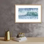 ‘Coastal Wave’ framed on the wall of a minimalist living room, offering a serene and dynamic beach scene in soothing blues and greens.