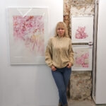 Kateryna Nazarenko beside her 'Pink Opuntia Cactus' watercolor painting displayed at an art exhibition, showcasing the soft pastel tones and intricate details of the botanical artwork in a serene, modern setting.