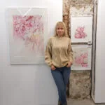 Kateryna Nazarenko beside her 'Pink Opuntia Cactus' watercolor painting displayed at an art exhibition, showcasing the soft pastel tones and intricate details of the botanical artwork in a serene, modern setting.