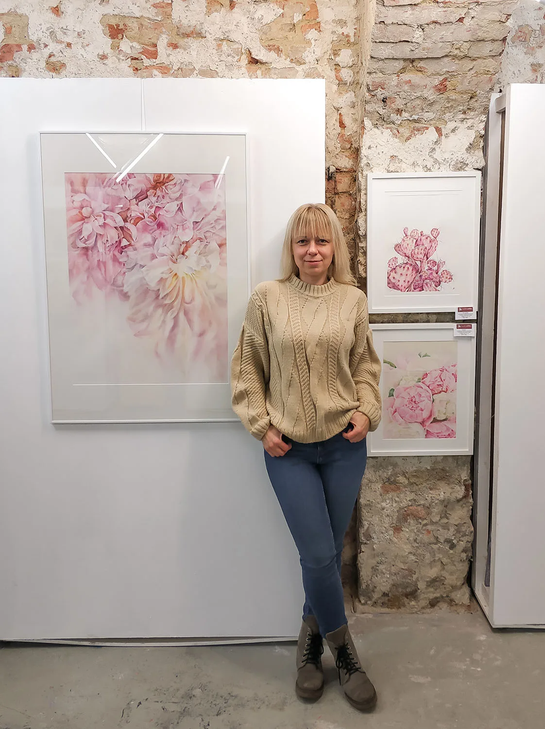 Kateryna Nazarenko beside her 'Pink Opuntia Cactus' watercolor painting displayed at an art exhibition, showcasing the soft pastel tones and intricate details of the botanical artwork in a serene, modern setting.