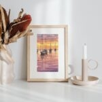 Framed small watercolor paintings of Resting Sailboats at Sunset displayed on a shelf, capturing peaceful sailboats on still waters beneath a warm sunset sky, creating a calming and serene atmosphere in any room.