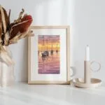 Framed small watercolor paintings of Resting Sailboats at Sunset displayed on a shelf, capturing peaceful sailboats on still waters beneath a warm sunset sky, creating a calming and serene atmosphere in any room.