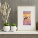 Resting Sailboats at Sunset small watercolor painting framed on a shelf, showing tranquil sailboats on calm waters with a sunset sky reflecting in the ocean, creating a serene coastal atmosphere.
