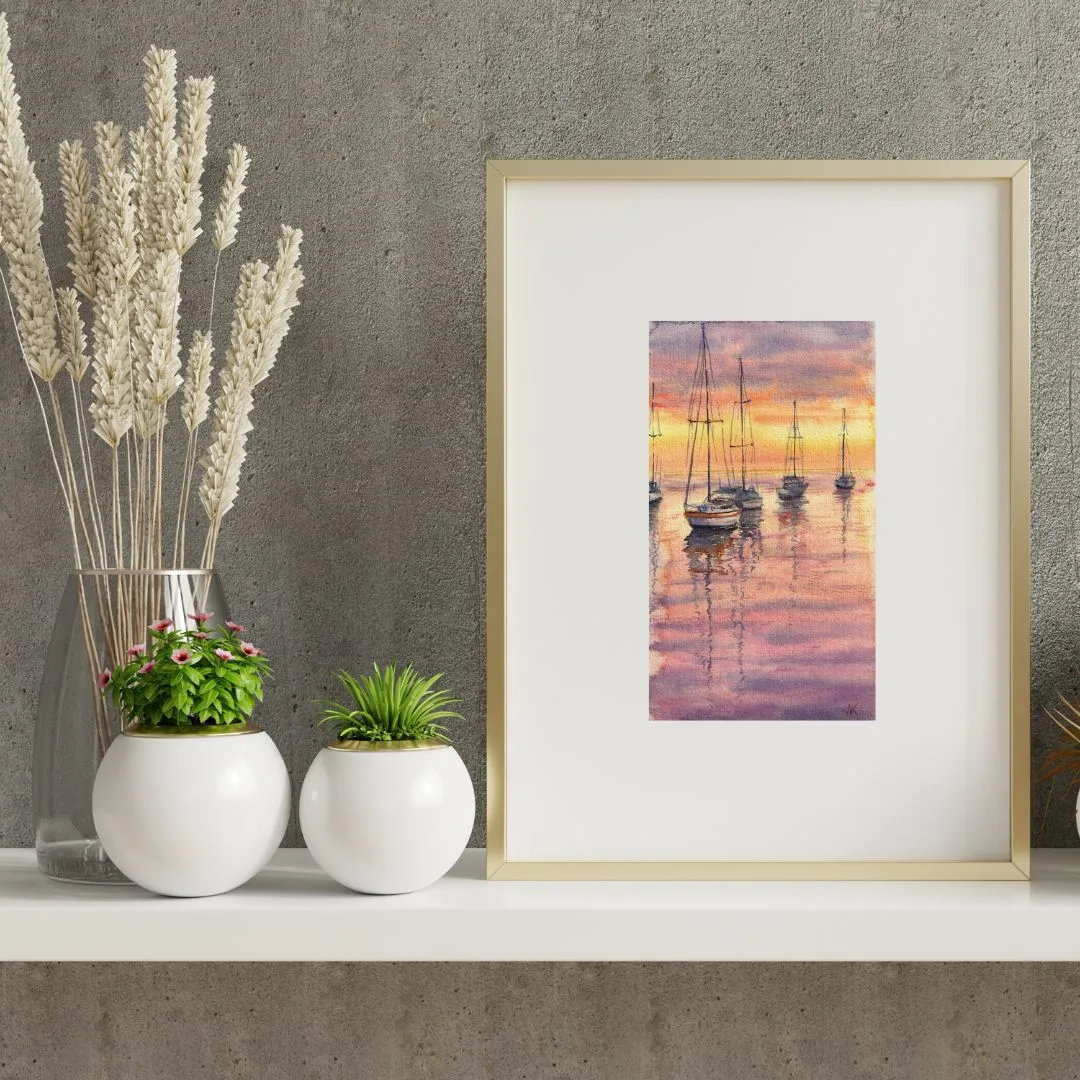 Resting Sailboats at Sunset small watercolor painting framed on a shelf, showing tranquil sailboats on calm waters with a sunset sky reflecting in the ocean, creating a serene coastal atmosphere.