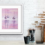Watercolor painting "Sailboats at Pink Sunset" by Kateryna Nazarenko displayed above a working desk, featuring soft pink and lavender hues and peaceful sailboats on still water.