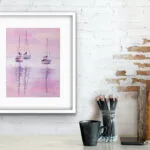 Watercolor painting "Sailboats at Pink Sunset" by Kateryna Nazarenko displayed above a working desk, featuring soft pink and lavender hues and peaceful sailboats on still water.