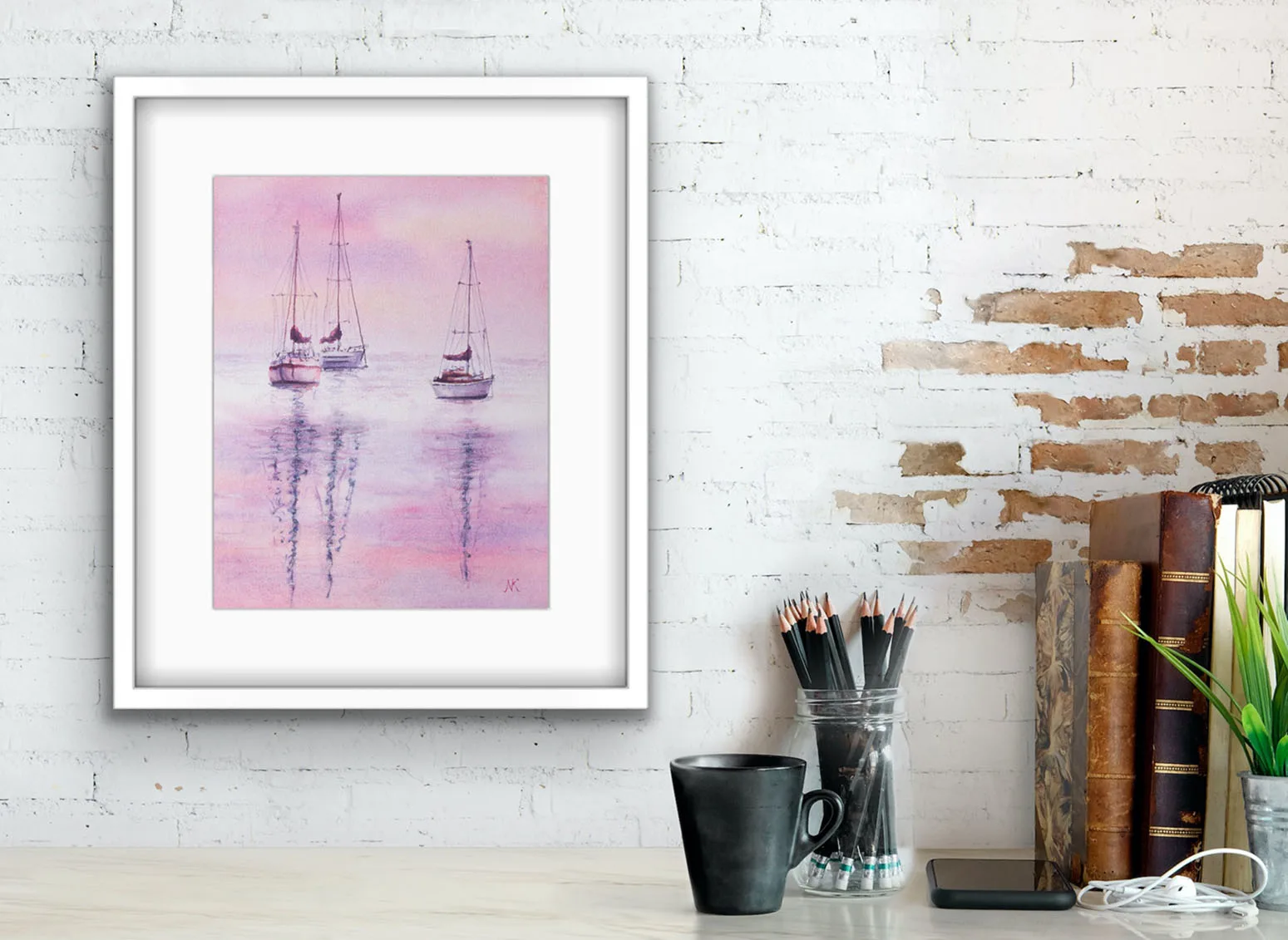 Watercolor painting "Sailboats at Pink Sunset" by Kateryna Nazarenko displayed above a working desk, featuring soft pink and lavender hues and peaceful sailboats on still water.