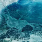 Closeup of the crashing wave in 'Through the Light' watercolor, showing the translucent water and intricate texture of the foam, highlighting the play of light on the ocean's surface.