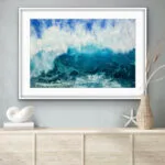 Framed 'Through the Light' watercolor painting displayed above a shelf with coastal decor, showcasing a dynamic ocean wave in deep blues and turquoise, capturing the movement and serenity of the sea