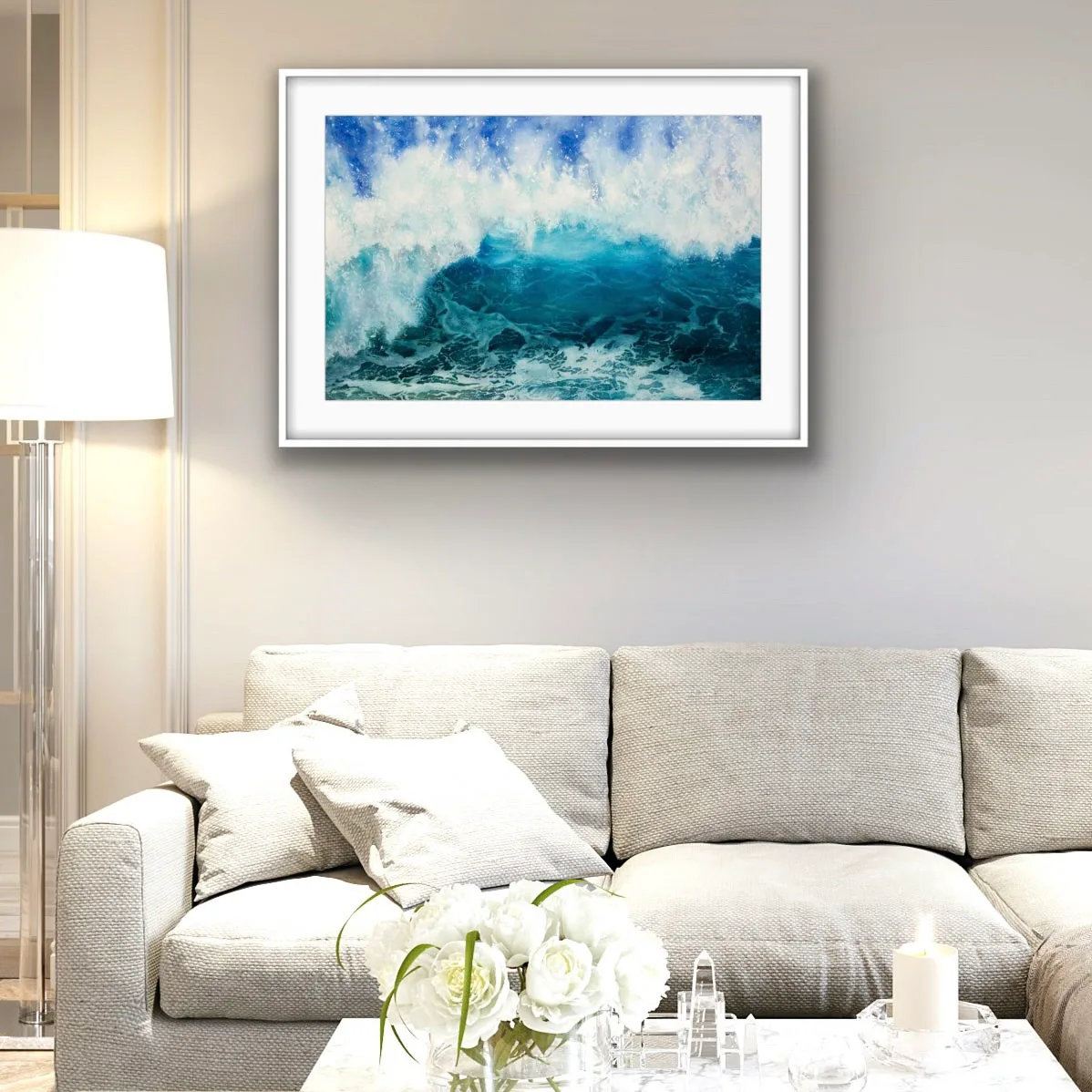 Framed 'Through the Light' watercolor painting above a sofa in a coastal living room, capturing the motion of a powerful ocean wave in deep blues and turquoise, enhancing the serene yet dynamic coastal ambiance of the space.