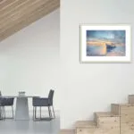 "Morning Solitude" painting displayed above a staircase, bringing a peaceful coastal vibe to the space.
