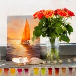 Sailing into the Sunset watercolor painting displayed on a studio window with soft natural light and fresh flowers, enhancing its serene coastal ambiance.