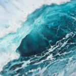 Close-up of ocean wave spray with frothy white foam and blue tones.