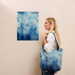 Stylish woman holding the Blue Ocean Tote Bag beside ocean wall art – a perfect pairing of abstract seascape fashion and coastal home decor, ideal for ocean art collectors and lovers of serene beach aesthetics.