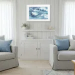 Framed Blue Ocean Whisper in light wood interior, modern ocean painting for coastal living room, soft wave movement and sea-inspired tones.