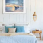 Watercolor seascape print Morning Solitude featuring a calm sea at sunrise with a boat, styled in a light coastal bedroom with ocean-inspired wall art and soft natural tones.