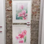 Pink Magnolias framed and displayed at an art exhibition, emphasizing its soft pink and green botanical color palette.