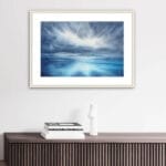 "Where Storm Meets Light" watercolor painting of a stormy blue ocean with glowing light, displayed in a living room. This marine-inspired seascape artwork adds a dramatic and calming focal point to the coastal decor, enhancing the space with ocean wall art elegance.