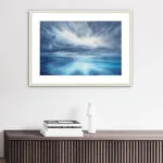 "Where Storm Meets Light" watercolor painting of a stormy blue ocean with glowing light, displayed in a living room. This marine-inspired seascape artwork adds a dramatic and calming focal point to the coastal decor, enhancing the space with ocean wall art elegance.
