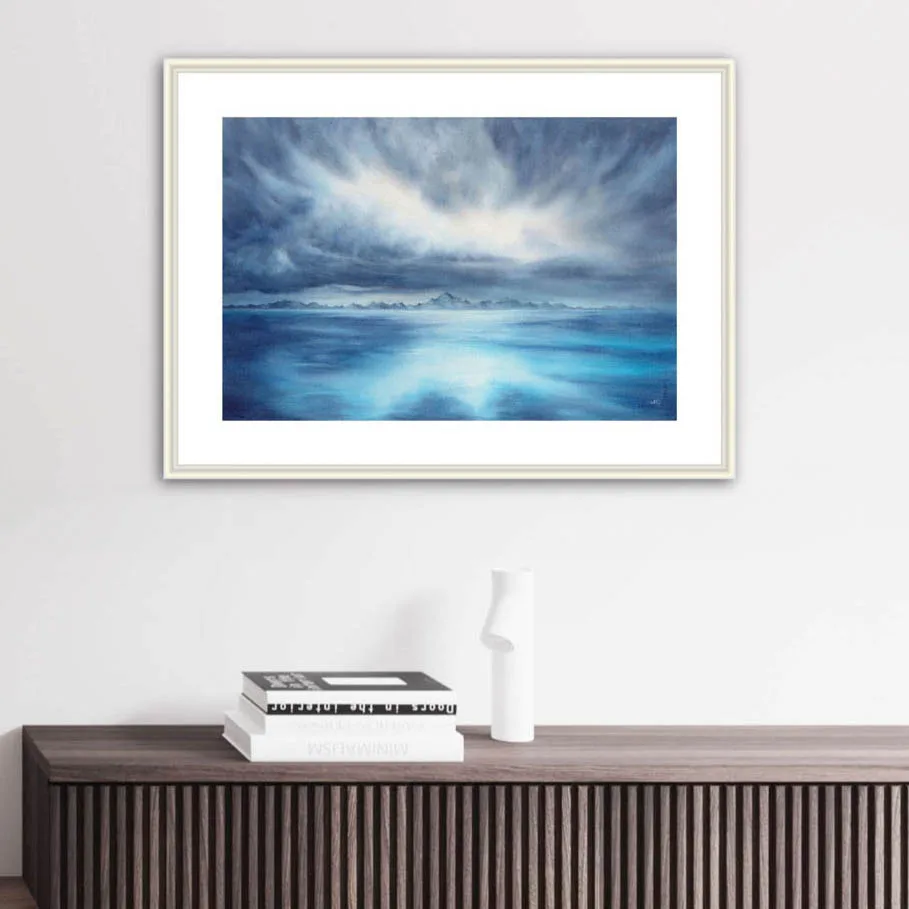 "Where Storm Meets Light" watercolor painting of a stormy blue ocean with glowing light, displayed in a living room. This marine-inspired seascape artwork adds a dramatic and calming focal point to the coastal decor, enhancing the space with ocean wall art elegance.