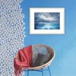 "Where Storm Meets Light" fine art print of a stormy sea watercolor painting displayed in a coastal interior. This blue ocean wall art adds a dynamic and calming element to the space, blending seamlessly with the light, airy decor and marine-inspired accents for a serene seascape focal point.