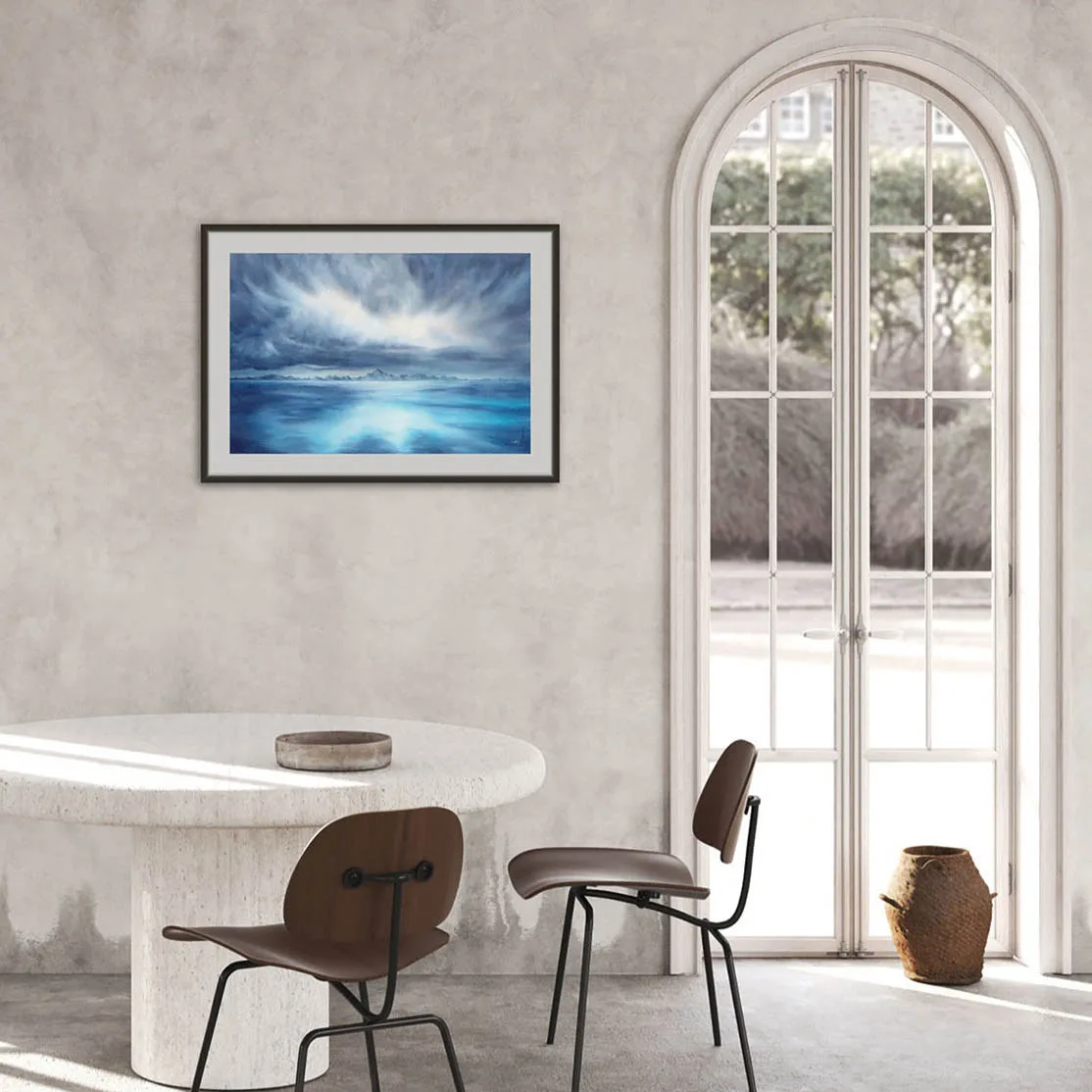 "Where Storm Meets Light" fine art print of a stormy sea watercolor painting displayed in a contemporary loft home. This blue ocean wall art adds a bold, dramatic touch to the open, modern space, enhancing the industrial and coastal-inspired decor with a serene yet powerful seascape focal point.