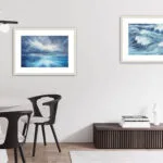 "Where Storm Meets Light" fine art print of a stormy sea watercolor painting displayed in a living room dining area. This blue ocean wall art serves as a captivating focal point, enhancing the open, airy space with its dramatic seascape and coastal-inspired decor.