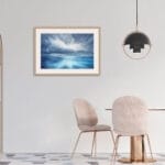 "Where Storm Meets Light" fine art print of a stormy sea watercolor painting displayed in a contemporary dining room. This blue ocean wall art adds a touch of elegance and drama, complementing the modern dining space with a seascape that brings nature's beauty to the table.