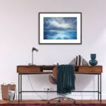 "Where Storm Meets Light" fine art print of a stormy sea watercolor painting displayed in a home office. This blue ocean wall art adds a calming, yet dramatic touch to the workspace, enhancing the modern, coastal-inspired decor with a peaceful seascape focal point.