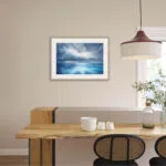 "Where Storm Meets Light" fine art print of a stormy sea watercolor painting displayed in a coastal kitchen. This blue ocean wall art brings a touch of tranquility and natural beauty to the space, complementing the marine-inspired decor and light-filled kitchen atmosphere.