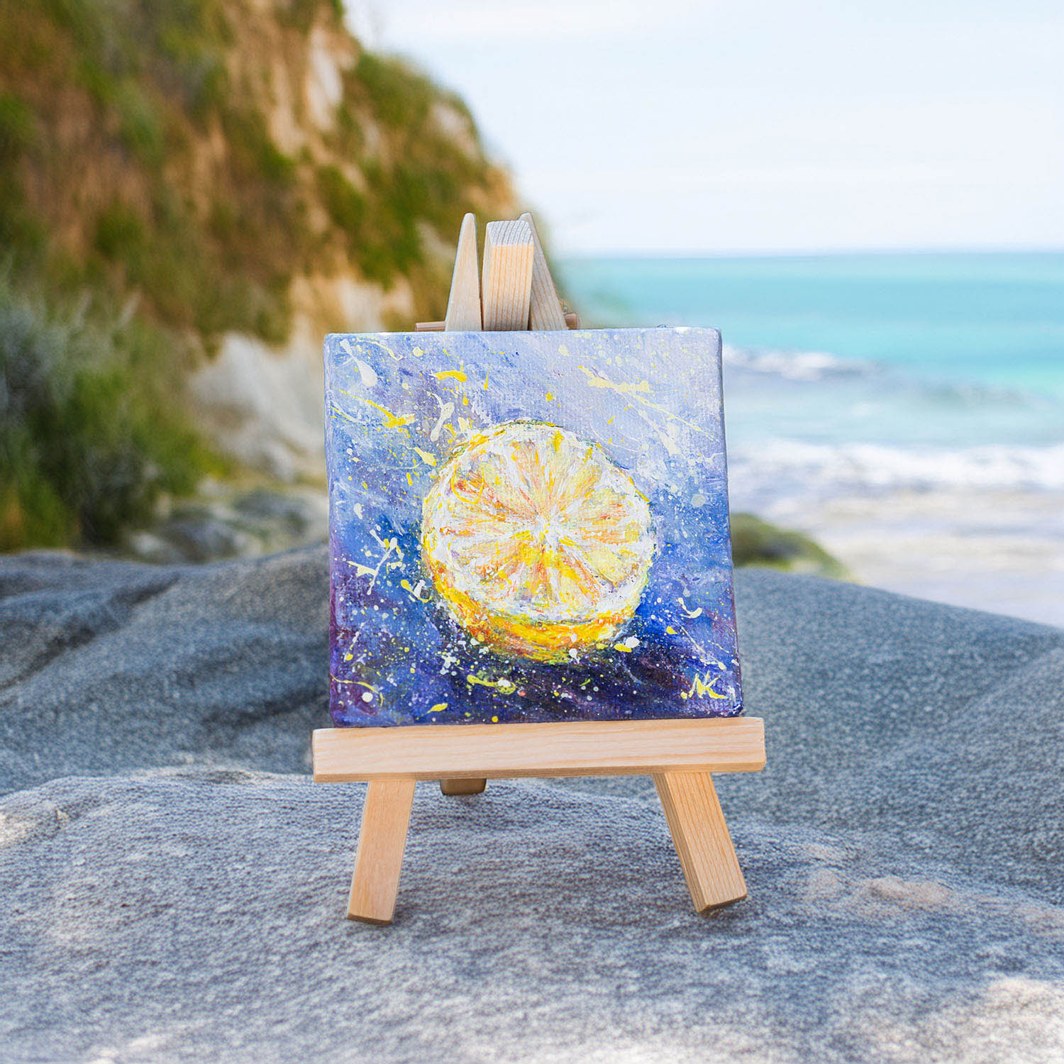 Original miniature acrylic painting of a bright lemon slice on blue canvas displayed on a wooden easel.
